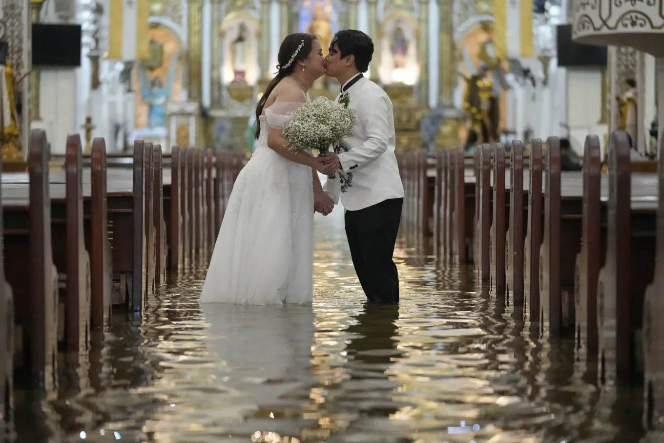 Newlyweds Jade Rick Verdillo right, and Jamaica kiss during their wedding at the flooded Barasoain church in Malolos, Bulacan province, Philippines on Tuesday, July 22, 2025.

