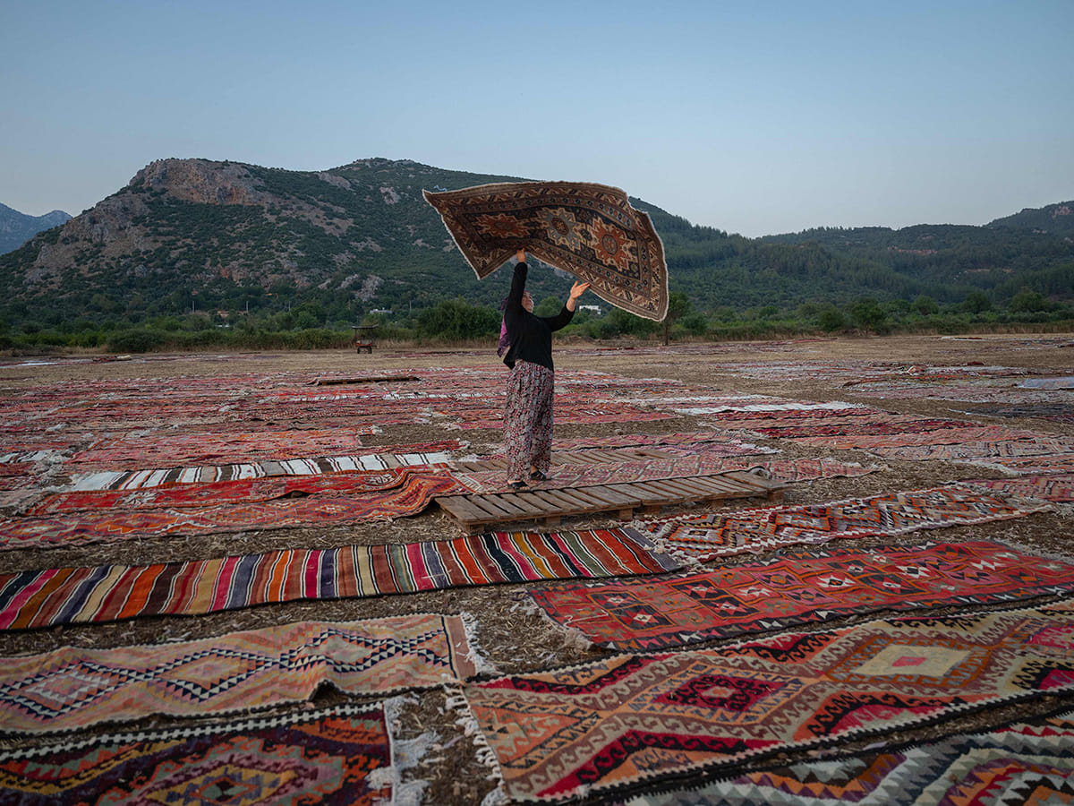 A worker holds an handwoven carpet laid out in an open field to soften its colours under sizzling sun in Dosemealti district in Antalya on July 22, 2025.