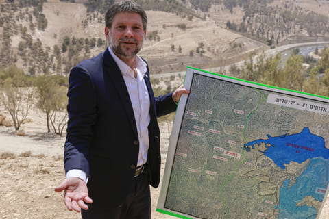 Israeli far-right Finance Minister Bezalel Smotrich holds a map of an area near the settlement of Maale Adumim, a land corridor known as E1, outside Jerusalem in the occupied West Bank, on August 14, 2025, after a press conference at the site.
