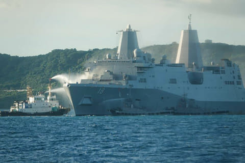 This handout photo taken on August 20, 2025 and received on August 21, 2025 from the Japan Coast Guard shows smoke coming from the US Navy vessel USS New Orleans as water is sprayed (L) to help put out the fire, off the coast near White Beach on the Japanese southern island of Okinawa.