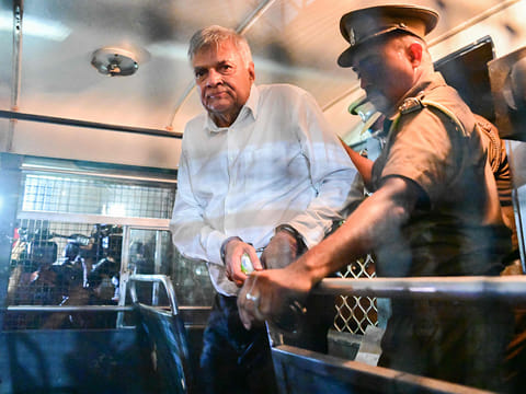 Sri Lanka's former president Ranil Wickremesinghe is escorted to his seat in a prison bus in Colombo on August 22, 2025, after a magistrate ordered him to be held in remand custody till August 26, 2025, following allegations that he misused state funds to travel to Britain in 2023. 