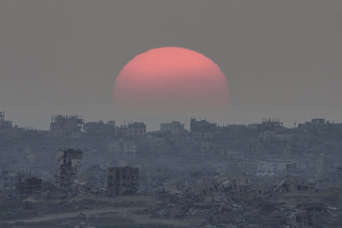 The sun sets behind buildings destroyed during Israeli ground and air operations in the Gaza Strip, as seen from southern Israel, Tuesday, August 26, 2025. 