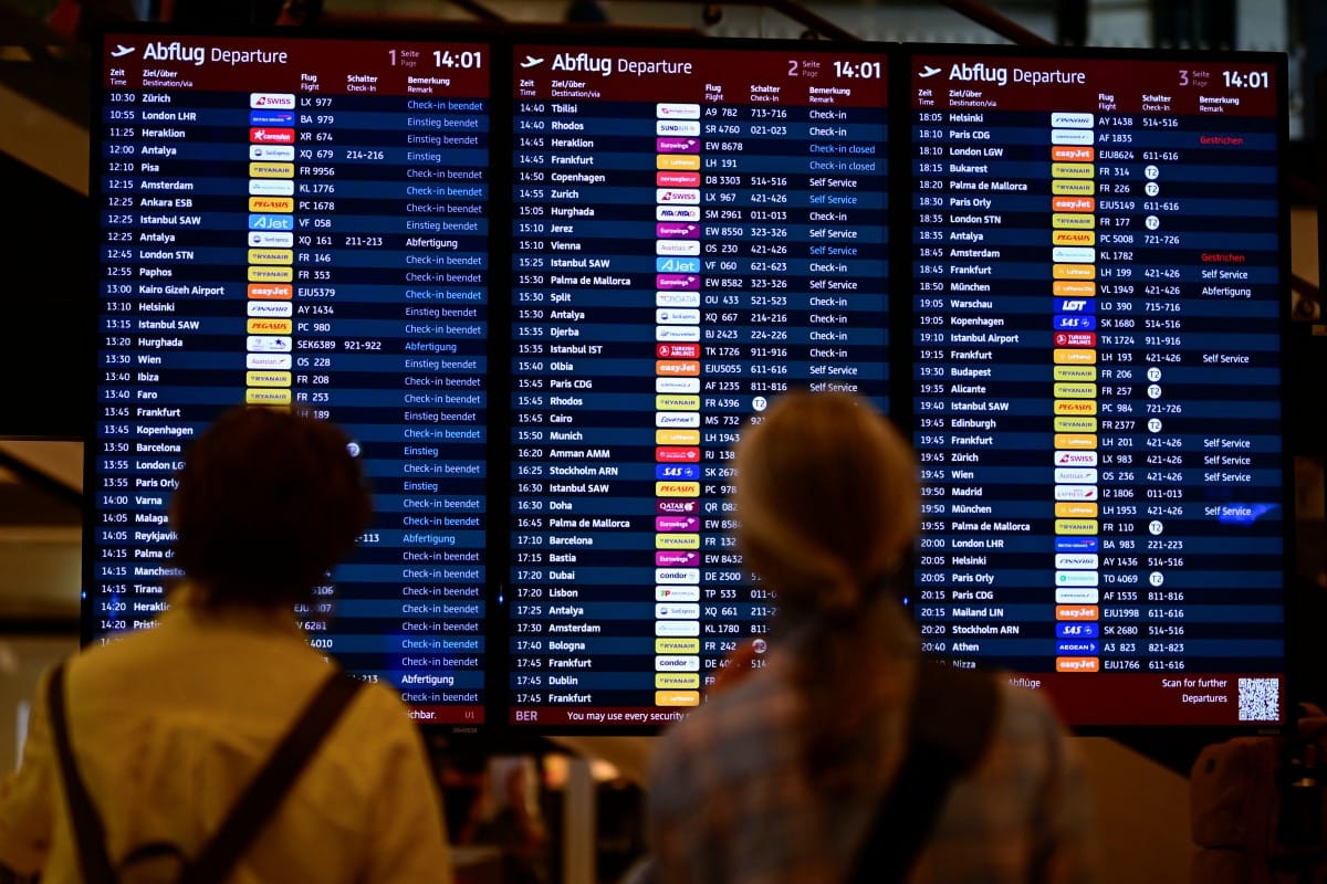 Passengers check a digital display showing status of outgoing and incoming flights.