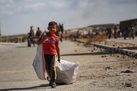 A Palestinian boy carries a bag and drags another behind him as he returns from a food distribution point run by the US and Israeli-backed Gaza Humanitarian Foundation (GHF) group, near the Netsarim corridor in the central Gaza Strip on October 5, 2025.