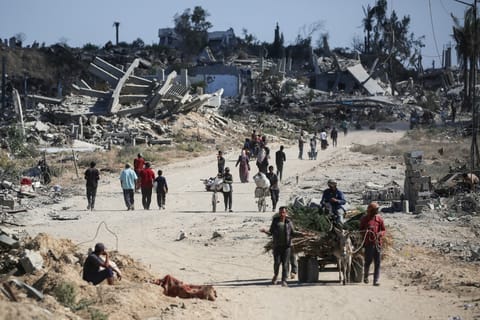 Displaced Palestinians walk past destroyed buildings as they return to their homes in the Al Zahra area, north of the Nuseirat refugee camp in the central Gaza Strip, on October 14, 2025, a day after a ceasefire came into effect.