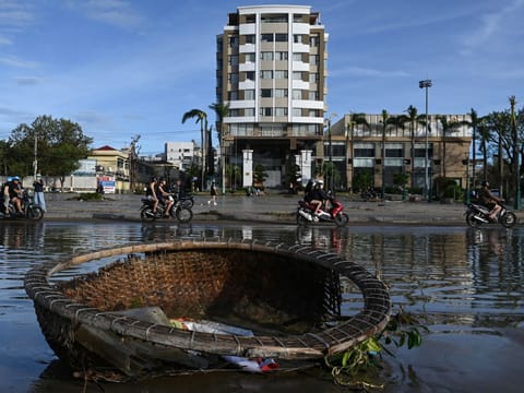 Motorists ride past pools of water and a coracle boat swept inland by typhoon Kalmaegi in Quy Nhon in Gia Lai province, central Vietnam on November 7, 2025.