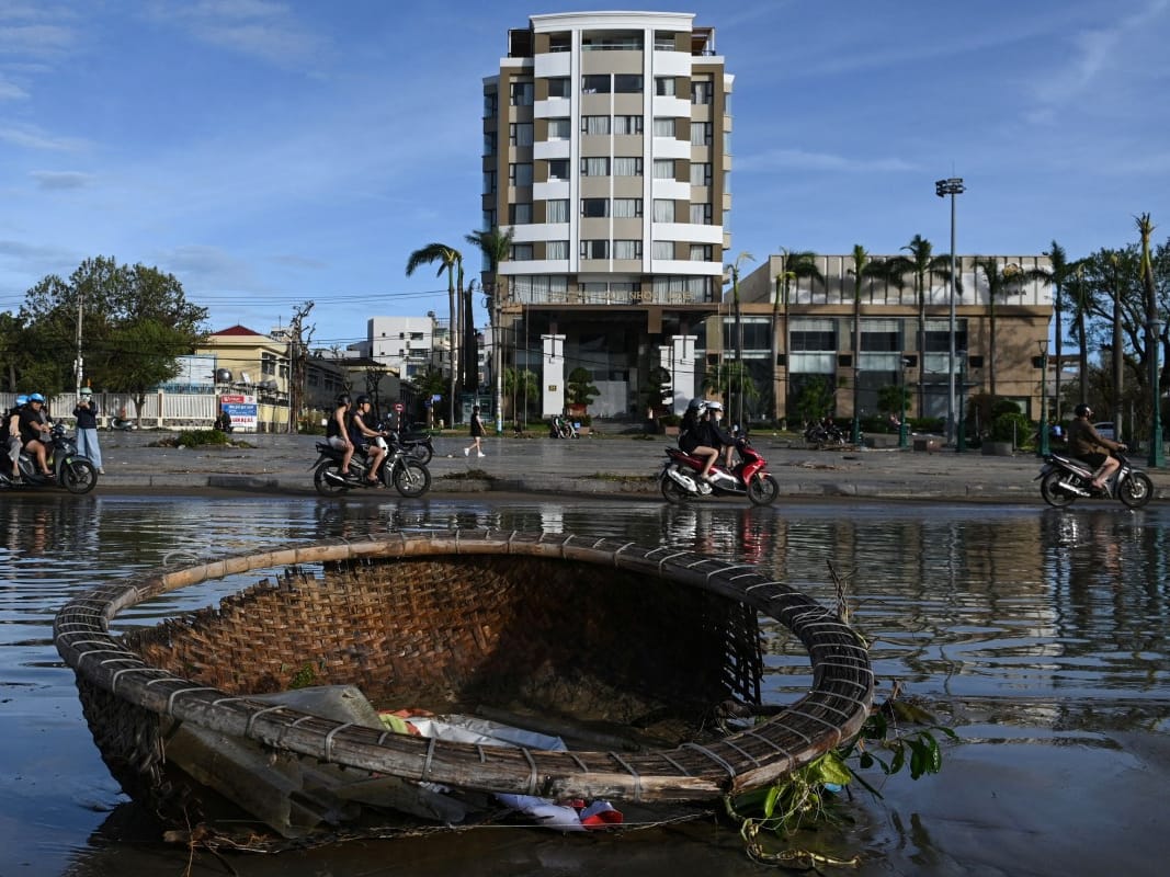 Motorists ride past pools of water and a coracle boat swept inland by typhoon Kalmaegi in Quy Nhon in Gia Lai province, central Vietnam on November 7, 2025.