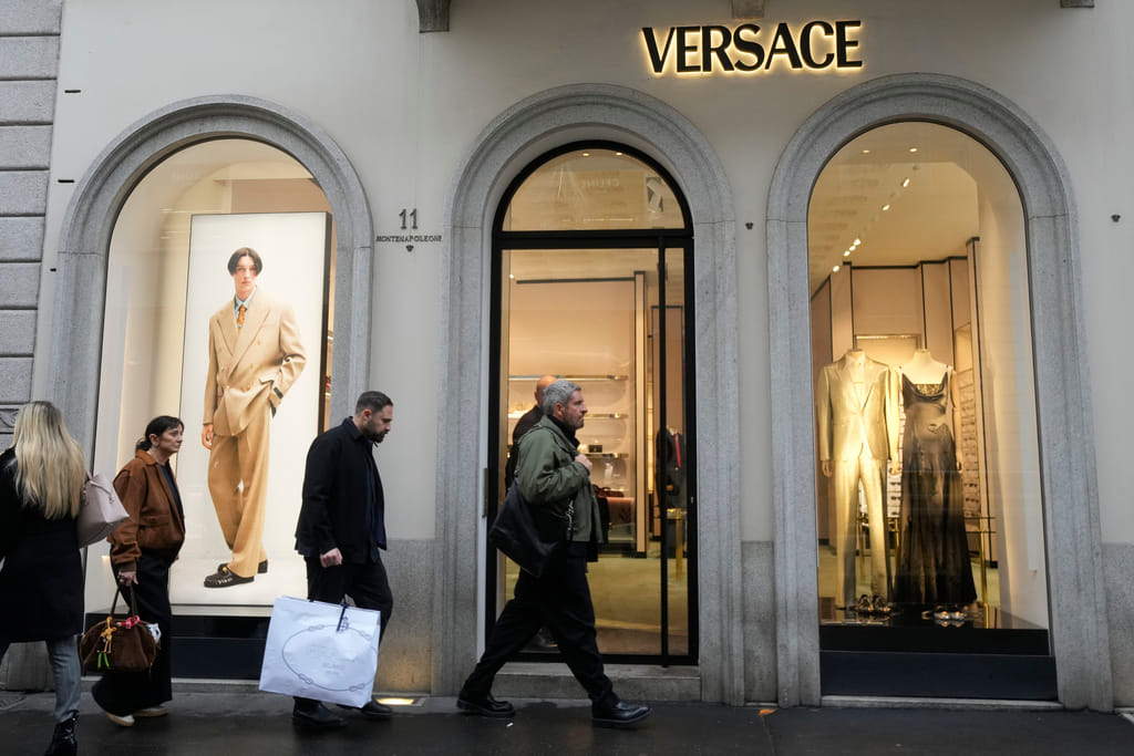 A man walks with a Prada shopping bag in front of a Versace shop, at the Montenapoleone luxury fashion street, in Milan, Italy.