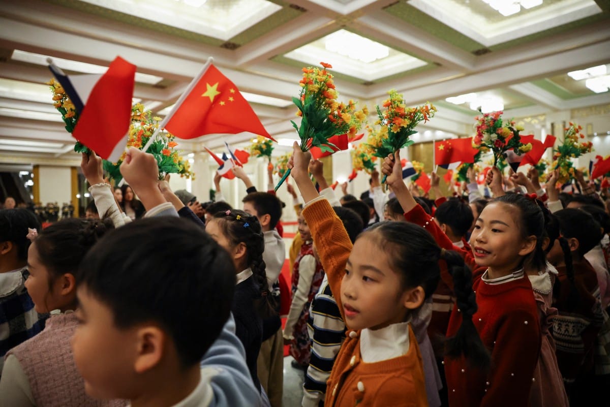 Children wave Chinese flags and hold up flowers at the Great Hall of the People in Beijing on December 4, 2025.