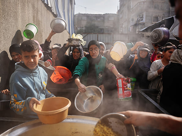 Palestinian women struggle to receive donated food at a community kitchen in Nuseirat, central Gaza Strip. 
