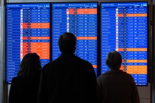 Travelers look at a flight status board as flights are delayed and cancelled.