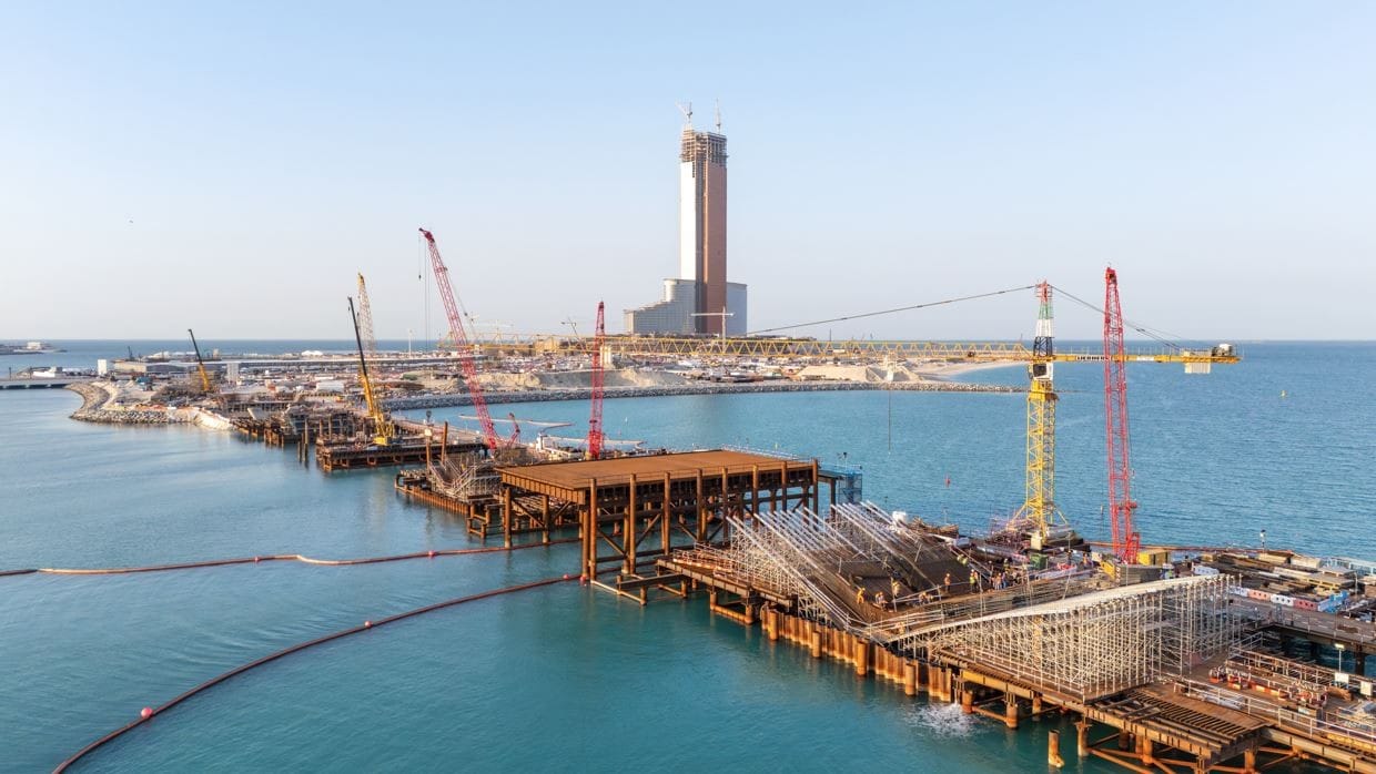 An under-construction bridge linking Wynn Al Marjan Island to the UAE road network, with pillars and decking visible during daytime works in Ras Al Khaimah.