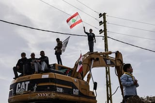 Standing on a digger used to clear the rubble of destroyed homes and businesses, a Lebanese youth holds up the Lebanese flag as residents wait for the arrival of Lebanon's prime minister during his visit to the heavily-damaged southern village of Kfar Shouba, near the border with Israel on February 8, 2026.