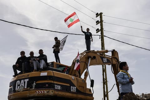 Standing on a digger used to clear the rubble of destroyed homes and businesses, a Lebanese youth holds up the Lebanese flag as residents wait for the arrival of Lebanon's prime minister during his visit to the heavily-damaged southern village of Kfar Shouba, near the border with Israel on February 8, 2026.