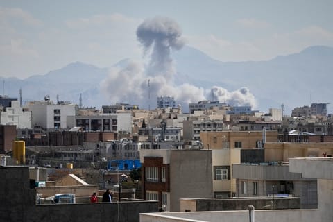 People watch from a rooftop as a plume of smoke rises after a strike in Tehran, Iran, Sunday, March 1, 2026. 