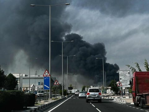 Motorists drive past a plume of smoke rising from a reported Iranian strike in the industrial district of Doha, Qatar, on March 1, 2026. 