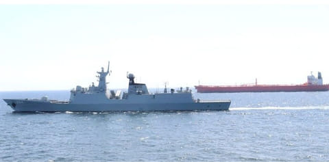 A naval vessel escorts a merchant ship. 