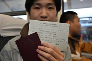 A Chinese student holds his passport and a ticket from Dandong, China to Sinuiji, North Korea on board the K27 train bound to Pyongyang, at Beijing Railway Station in Beijing on March 12, 2026.