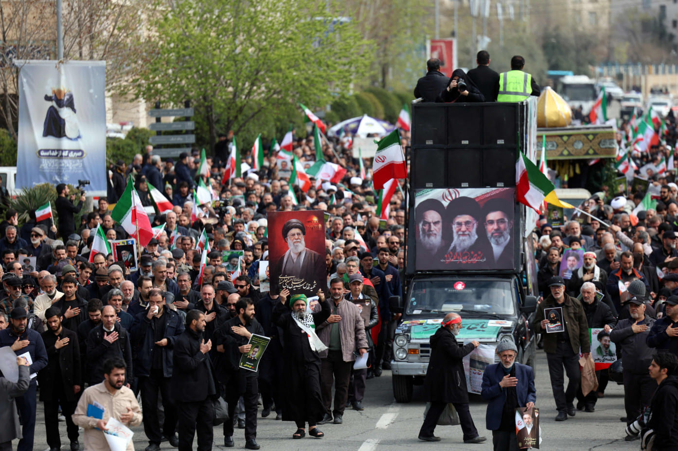A hearse decorated with pictures of Iranian spiritual leader Ayatollah Ruhollah Khomeini, Iran's slain supreme leader Ayatollah Ali Khamenei and Iran's new Supreme Leader Ayatollah Mojtaba Khamenei drives past Iranians attending the funeral ceremony of Iran's Revolutionary Guards spokesperson Ali Mohammad Naini, who was killed in US-Israeli strikes, in Tehran on March 21, 2026.  