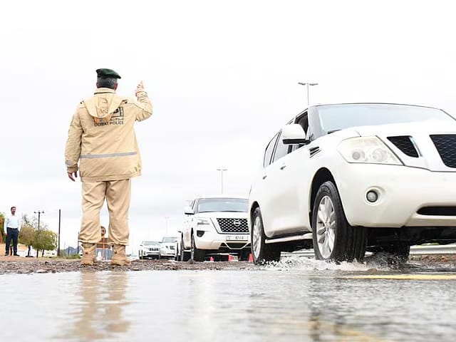 Dubai Police managing traffic on a road during the rain.