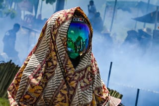 A helmeted participant looks on as others cook lemang, a traditional glutinous rice dish stuffed into bamboo tubes and filled with coconut milk which are then placed over an open fire, during a mass cooking event in Blang Pidie, Indonesia's Aceh province.