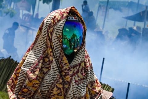A helmeted participant looks on as others cook lemang, a traditional glutinous rice dish stuffed into bamboo tubes and filled with coconut milk which are then placed over an open fire, during a mass cooking event in Blang Pidie, Indonesia's Aceh province.