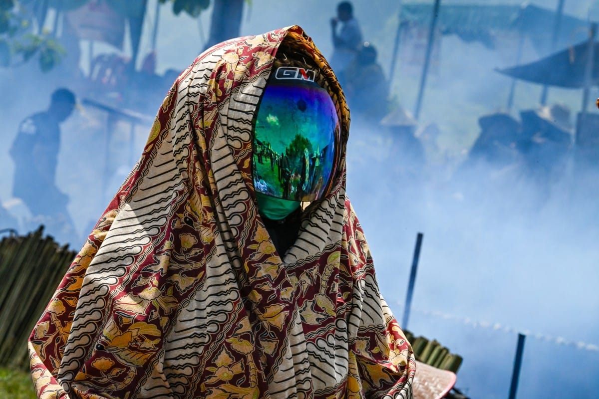 A helmeted participant looks on as others cook lemang, a traditional glutinous rice dish stuffed into bamboo tubes and filled with coconut milk which are then placed over an open fire, during a mass cooking event in Blang Pidie, Indonesia's Aceh province.