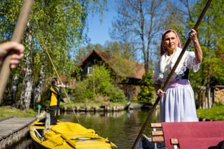 A woman wearing a traditional Sorb outfit (R) manouvers a so-called "Spreewaldkahn" barge carrying tourists along a canal in the Spreewald region in Luebbenau, eastern Germany, as in background can be seen a boat of the postal service.