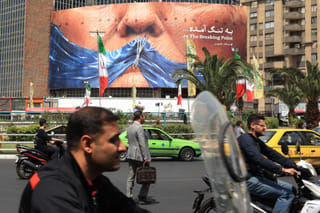 Commuters make their way past an anti-US billboard referring to President Donald Trump and the Strait of Hormuz, installed on a building at the Valiasr Square in Tehran on May 2, 2026. 