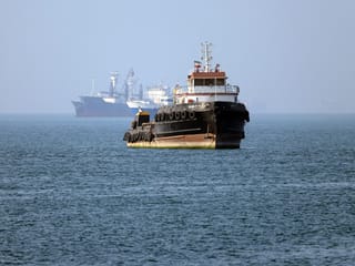 In this picture obtained from Iran's ISNA news agency on May 4, 2026, the Iran-flagged tugboat Basim sails near a ship anchored in the Strait of Hormuz off Bandar Abbas in southern Iran.