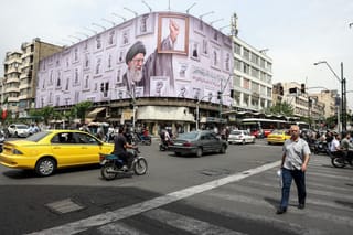 Iranians drive past a huge billboard carrying the image of the late Iranian supreme leader Ayatollah Ali Khamenei, killed in February 2026 in a military attack by the US and Israel on Iran, in a street in Tehran on May 5, 2026.