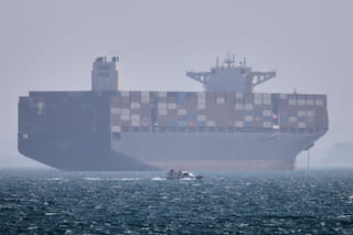A container ship sits at anchor as a small motorboat passes in the foreground in the Strait of Hormuz off Bandar Abbas, Iran, on Saturday, May 2, 2026. 