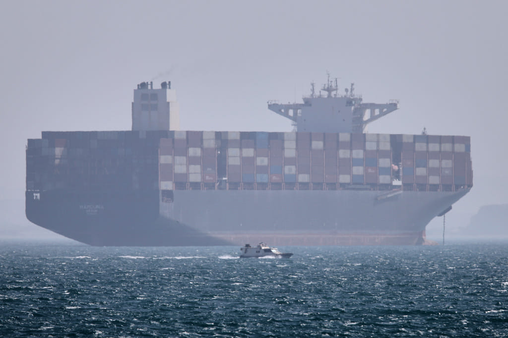 A container ship sits at anchor as a small motorboat passes in the foreground in the Strait of Hormuz off Bandar Abbas, Iran, on Saturday, May 2, 2026. 