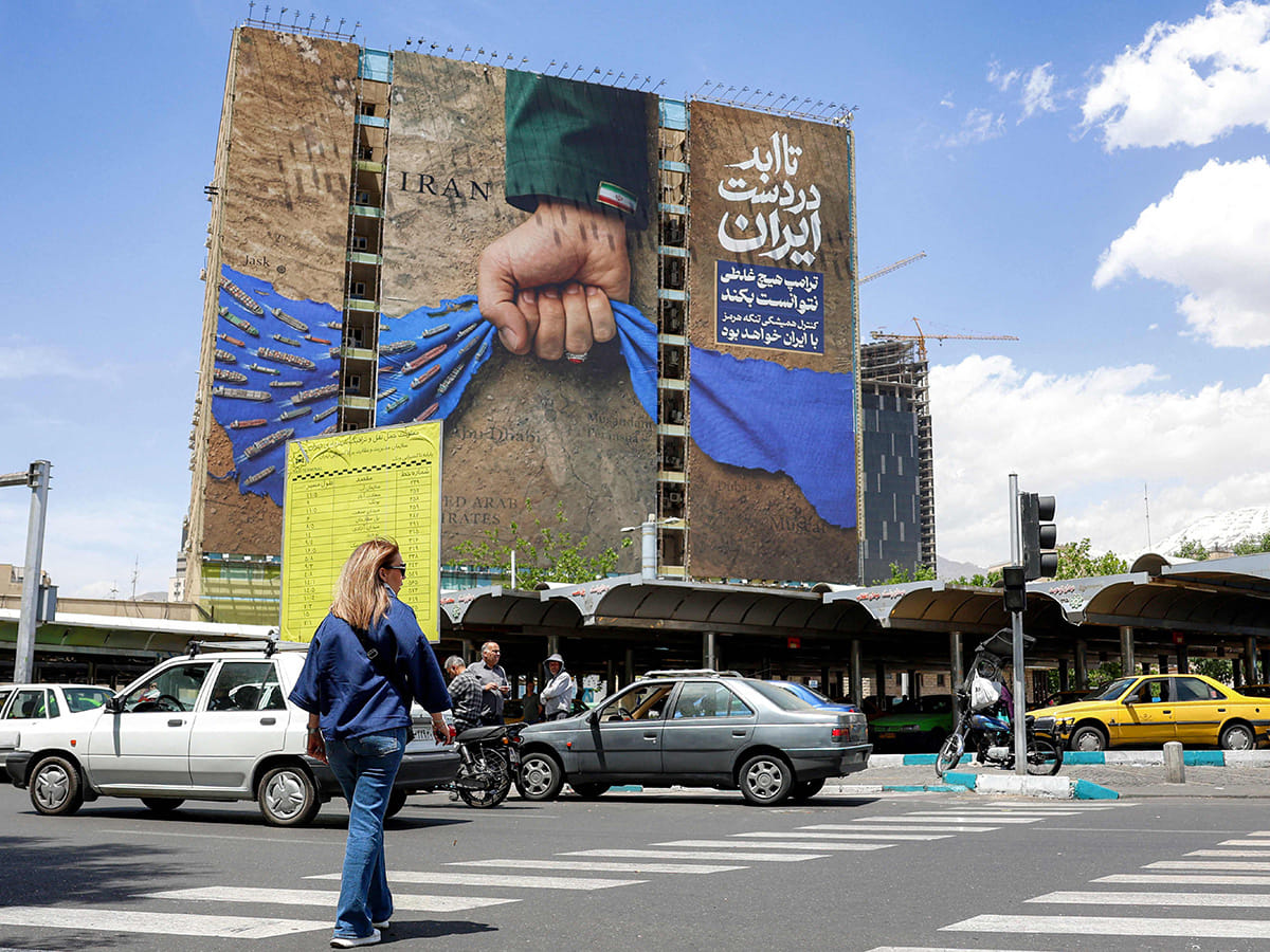 A woman crosses a street near a billboard on the facade of a building depicting the Strait of Hormuz with a caption in Persian reading 'Forever in Iran’s Hand', at Vanak Square in Tehran on May 6, 2026. 