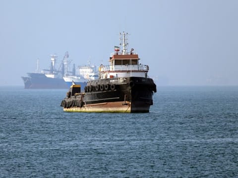 In this picture obtained from Iran's ISNA news agency on May 4, 2026, the Iran-flagged tugboat Basim sails near a ship anchored in the Strait of Hormuz off Bandar Abbas in southern Iran.