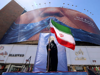 A woman holds the Iranian flag as she stands infront of an anti-US billboard referring to President Donald Trump and the Strait of Hormuz, installed on a building at the Valiasr Square in Tehran.