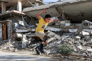 Akram al-Fayoumi, 13-year-old Palestinian amputee, performs a stunt while rollerblading past destroyed buildings with his prosthetic leg attachment along a street in Gaza City.