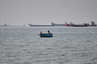 Two men sit in a small boat on the water as a mix of bulk carriers, cargo ships, and service vessels line the horizon in the Strait of Hormuz off Bandar Abbas, Iran, Monday, April 27, 2026.(Razieh Poudat/ISNA via AP)