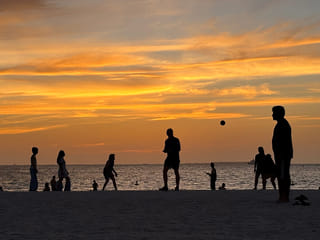 Manjula S. Dadallage captures a vibrant sunset scene at a Dubai beach, where silhouettes of people playing volleyball and enjoying the evening create a striking contrast against the glowing sky and calm shoreline.