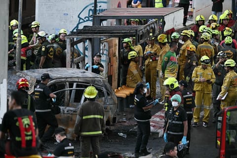 Forensic police officers, rescue workers and firefighters stand at the site of a train collision with a bus underneath Makkasan Airport Rail station in Bangkok on May 16, 2026.