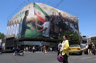 An Iranian woman waits to cross the intersection near a huge billboard supporting Iran’s national football team in the upcoming 2026 World Cup, installed on a building at Enghelab Square in Tehran on May 18, 2026.