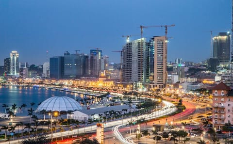 The Luanda glows along the Atlantic shoreline as waves roll in under night skies, where cranes and rising towers signal rapid construction while the Angolan capital’s waterfront pulses with vibrant nightlife and sea-breeze energy.