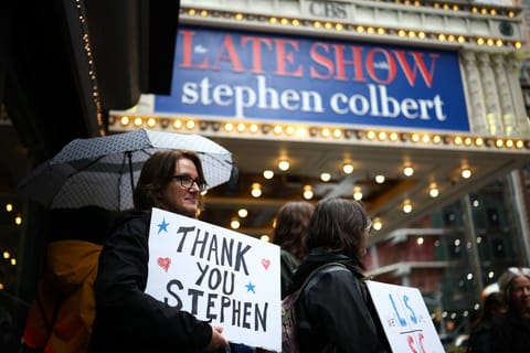 People hold signs supporting Stephen Colbert outside the Ed Sullivan Theater ahead of the taping of the final episode of the "The Late Show" after 32 years on air, in New York, on May 21, 2026.