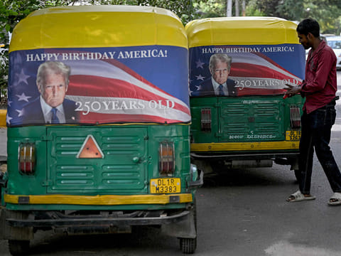 A worker fixes a poster featuring US President Donald Trump on an autorickshaw in New Delhi on May 21, 2026 marking the 250th anniversary of American independence.