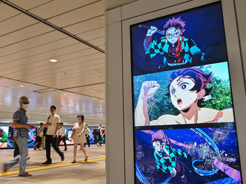 People walk past digital billboards advertising the upcoming release of the video game "Demon Slayer: Kimetsu no Yaiba – The Hinokami Chronicles 2"