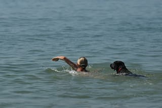 A swimmer and dog enjoy the cool sea temperatures off the beach in Brighton, on the south coast of England on May 25, 2026, as Monday is expected to be the hottest bank holiday ever, with heatwave conditions spreading to parts of southeast England and London.