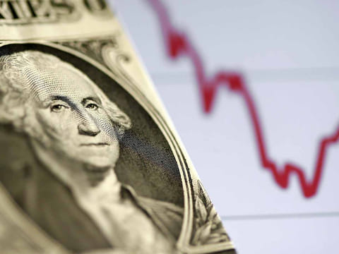 A US dollar note is seen in front of a stock graph. The dollar is facing renewed questions about its status as the globe's primary reserve currency.
