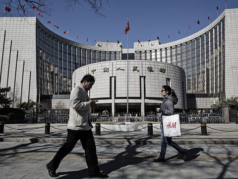 Pedestrians walk past the People's Bank of China (PBOC) headquarters in Beijing, China. Chinese small-cap stocks rallied after Premier Li Keqiang failed to mention a planned shift to a more market-based system for initial public offerings, a reform seen luring funds from existing equities. 