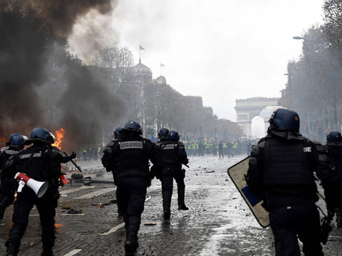Riot police run during a protest of Yellow vests (Gilets jaunes) against rising oil prices and living costs near the Arc of Triomphe on the Champs Elysees in Paris, on November 24, 2018.   Police fired tear gas and water cannon on November 24 in central Paris against "yellow vest" protesters demanding French President Emmanuel Macron roll back tax hikes on motor fuel. 