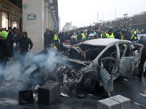 Demonstrators push charred car during a demonstration Saturday, Dec.1, 2018 in Paris. 